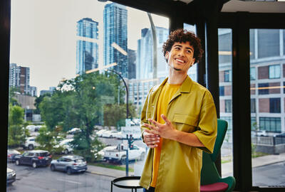 Male in yellow shirt standing at a window, smiling