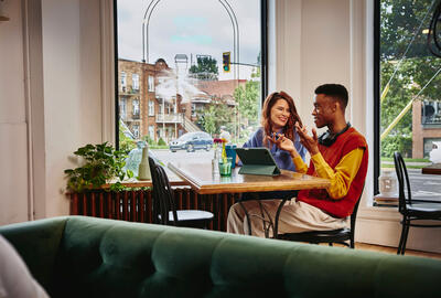 Man and woman sitting next to each other at a table in a cafe with a standing tablet.