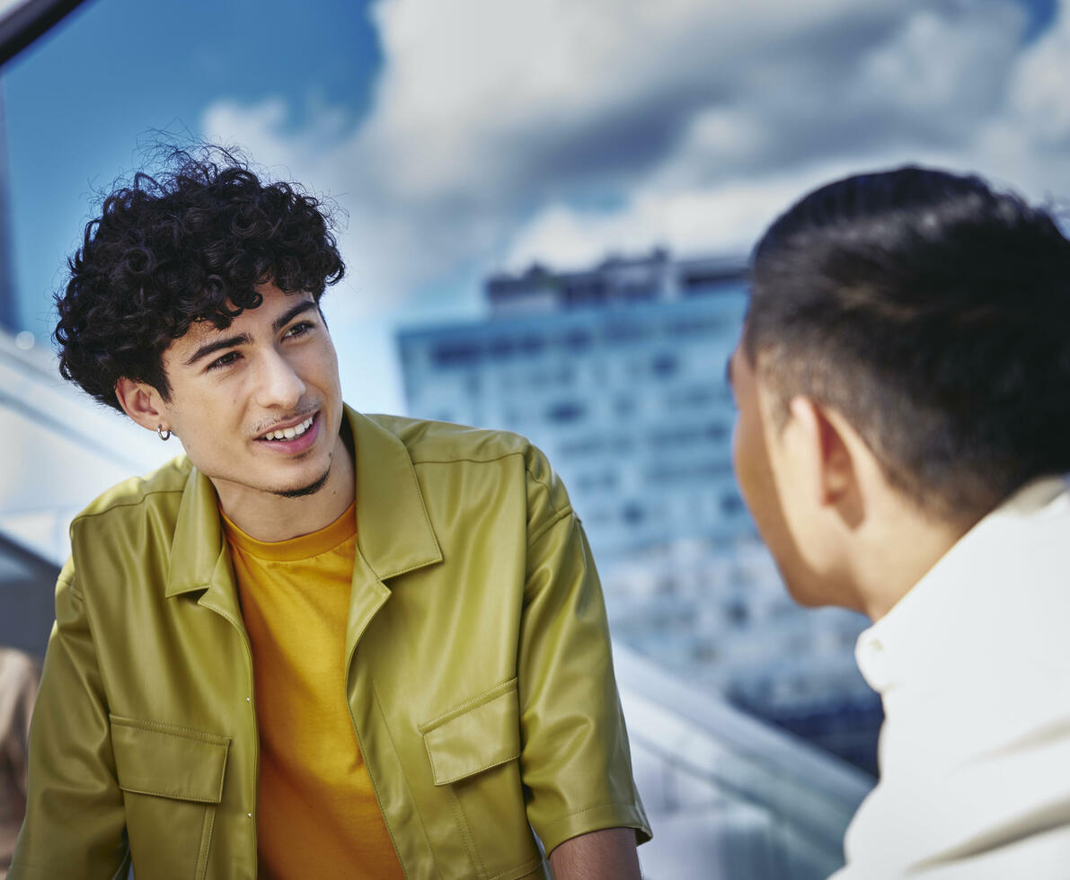 Male in yellow shirt and male, standing outside on a balcony, talking Male in yellow shirt and male, standing outside on a balcony, talking