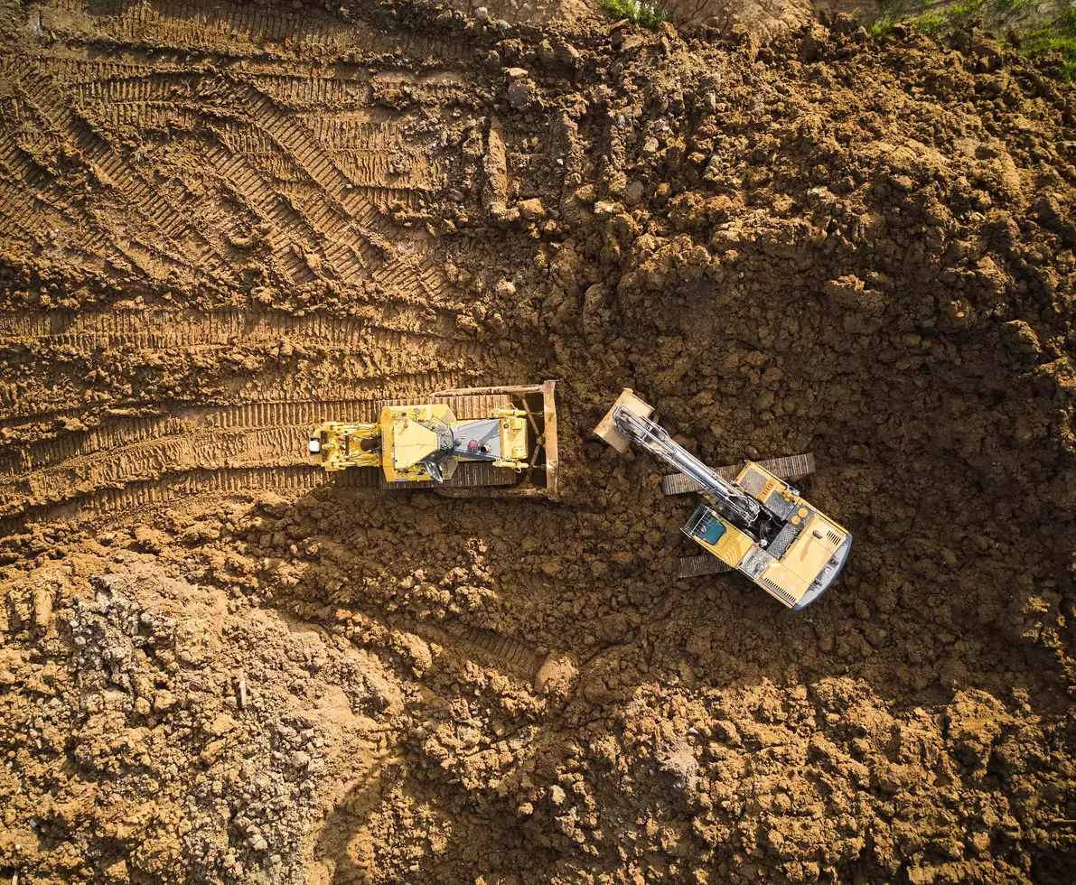 Bulldozer is scraping a layer of soil and excavator is digging and dumping dirt