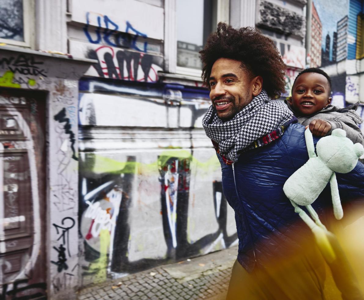 Smiling man with kid on his back walking through a city. Smiling man with kid on his back walking through a city.