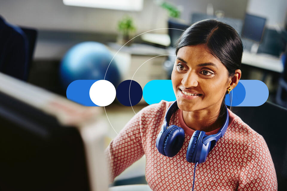 Woman with blue headphones around her neck looking at a screen.