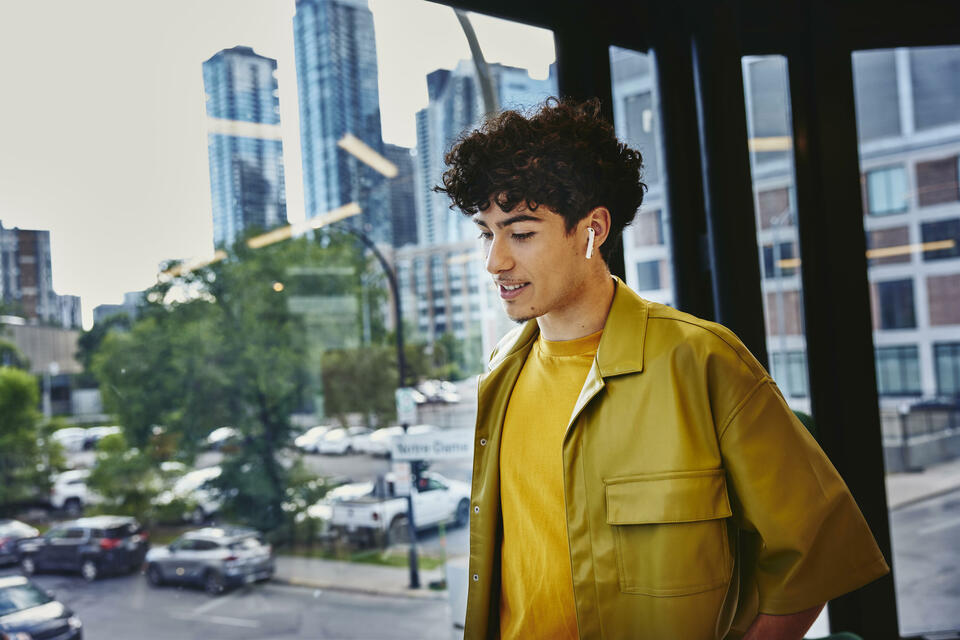 Male in yellow shirt, width earphones, standing at a window looking down Male in yellow shirt, width earphones, standing at a window looking down