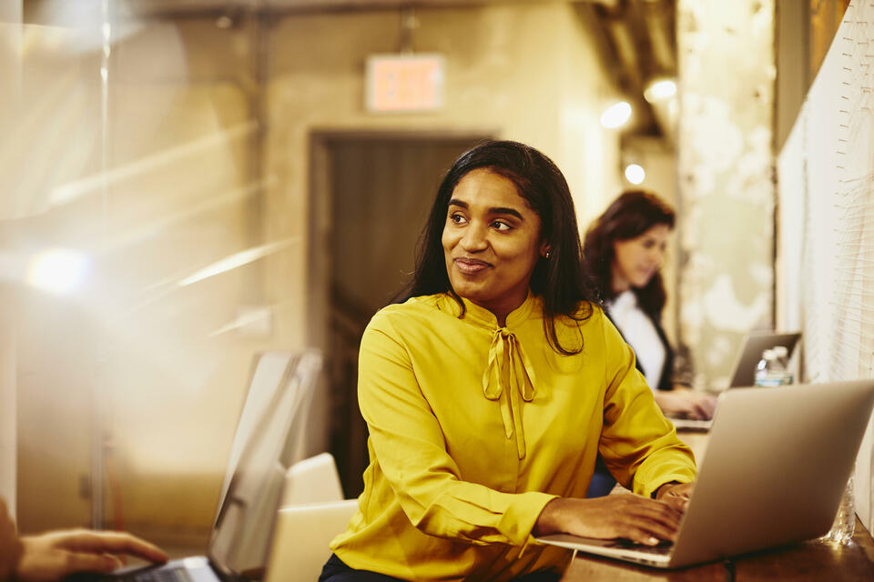 Two smiling female working on their laptop.
 Two smiling female working on their laptop.